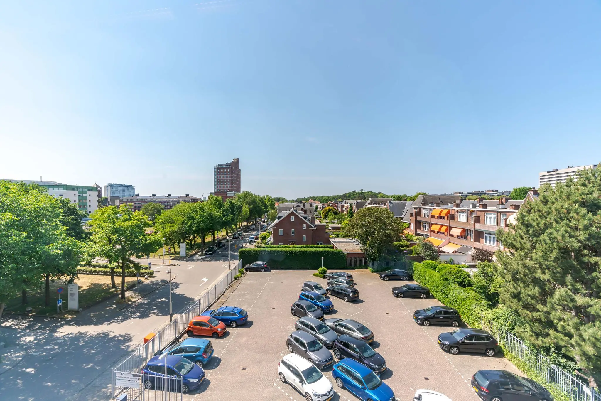 Uitzicht op de Van Alkemadelaan in Den Haag met een parkeerterrein op de voorgrond en woongebouwen en hoogbouw op de achtergrond.